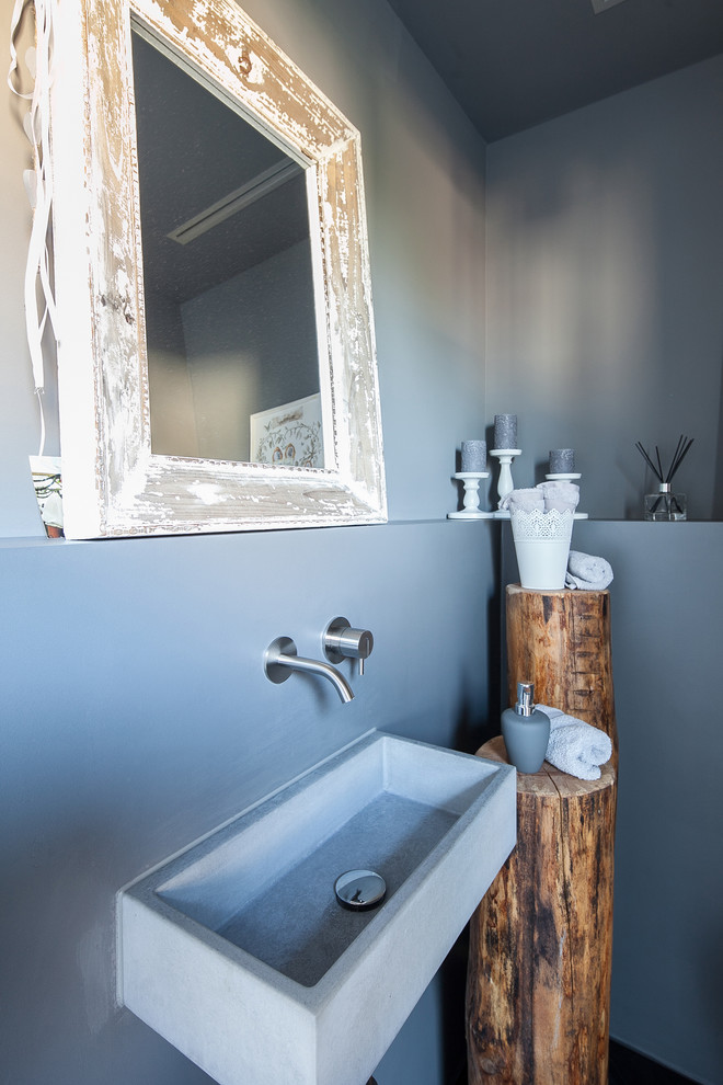 Photo of a mid-sized traditional powder room in Munich with grey walls, a wall-mount sink, concrete benchtops, open cabinets, white cabinets, a wall-mount toilet, blue tile, light hardwood floors and brown floor.