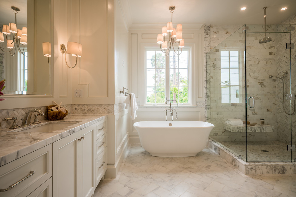 Inspiration for a large transitional master bathroom in Los Angeles with recessed-panel cabinets, white cabinets, a freestanding tub, a corner shower, marble, white walls, marble floors, an undermount sink, marble benchtops, a hinged shower door, white benchtops, beige tile, gray tile, white tile and white floor.