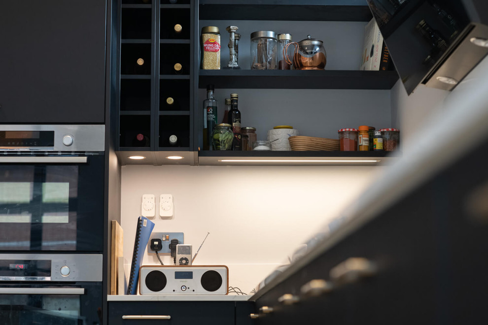Foto de cocina minimalista de tamaño medio con fregadero integrado, armarios con paneles lisos, puertas de armario negras, encimera de mármol, electrodomésticos negros, una isla, encimeras blancas y vigas vistas