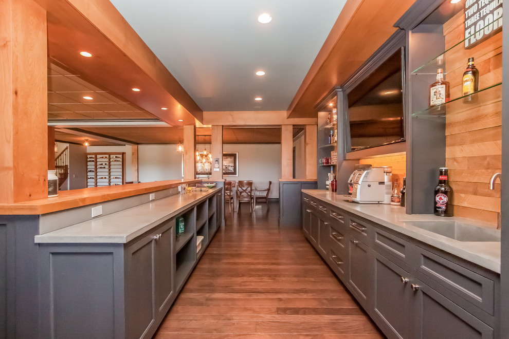 This is an example of a large arts and crafts galley wet bar in Boston with shaker cabinets, grey cabinets, medium hardwood floors, concrete benchtops, timber splashback, brown floor and grey benchtop.
