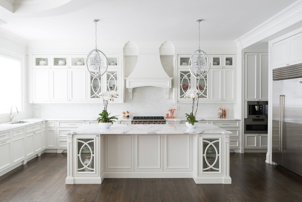 Traditional l-shaped kitchen in Toronto with a double-bowl sink, glass-front cabinets, white cabinets, marble benchtops, white splashback, stainless steel appliances, dark hardwood floors, with island, brown floor and white benchtop.