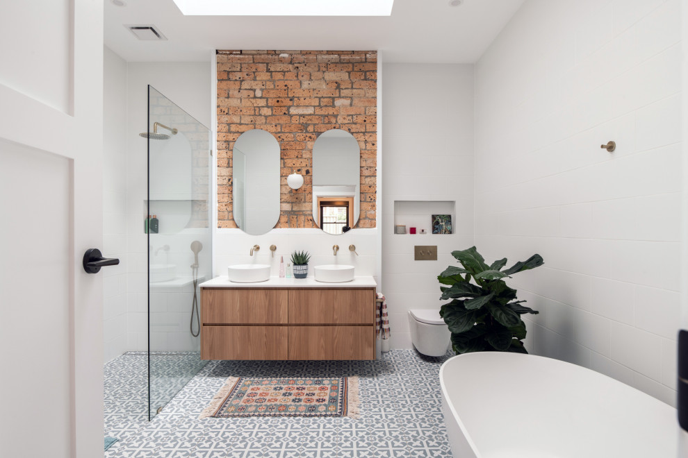 Inspiration for a contemporary bathroom in Sydney with flat-panel cabinets, medium wood cabinets, a freestanding tub, white tile, a vessel sink, grey floor, white benchtops, a double vanity, a floating vanity and brick walls.