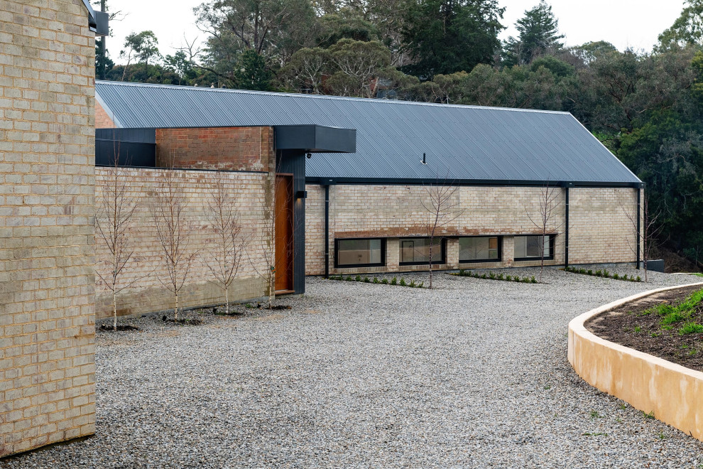Aménagement d'une grande façade de maison moderne en brique de plain-pied avec un toit à deux pans, un toit en métal et un toit gris.