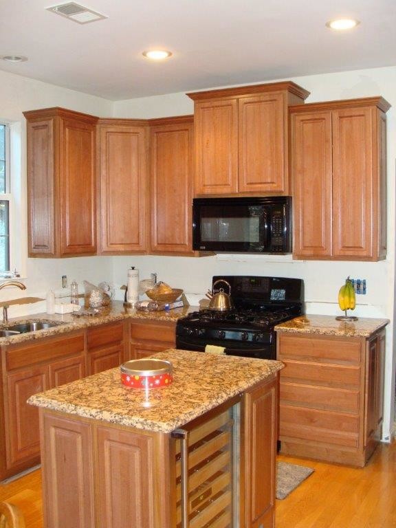 This is an example of a mid-sized traditional l-shaped kitchen in DC Metro with a double-bowl sink, raised-panel cabinets, medium wood cabinets, granite benchtops, black appliances, light hardwood floors and with island.