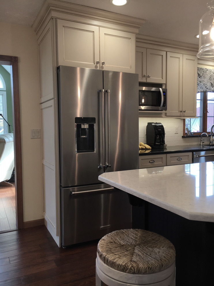 Example of a large transitional medium tone wood floor and brown floor eat-in kitchen design with an undermount sink, flat-panel cabinets, white cabinets, granite countertops, white backsplash, porcelain backsplash, stainless steel appliances and an island