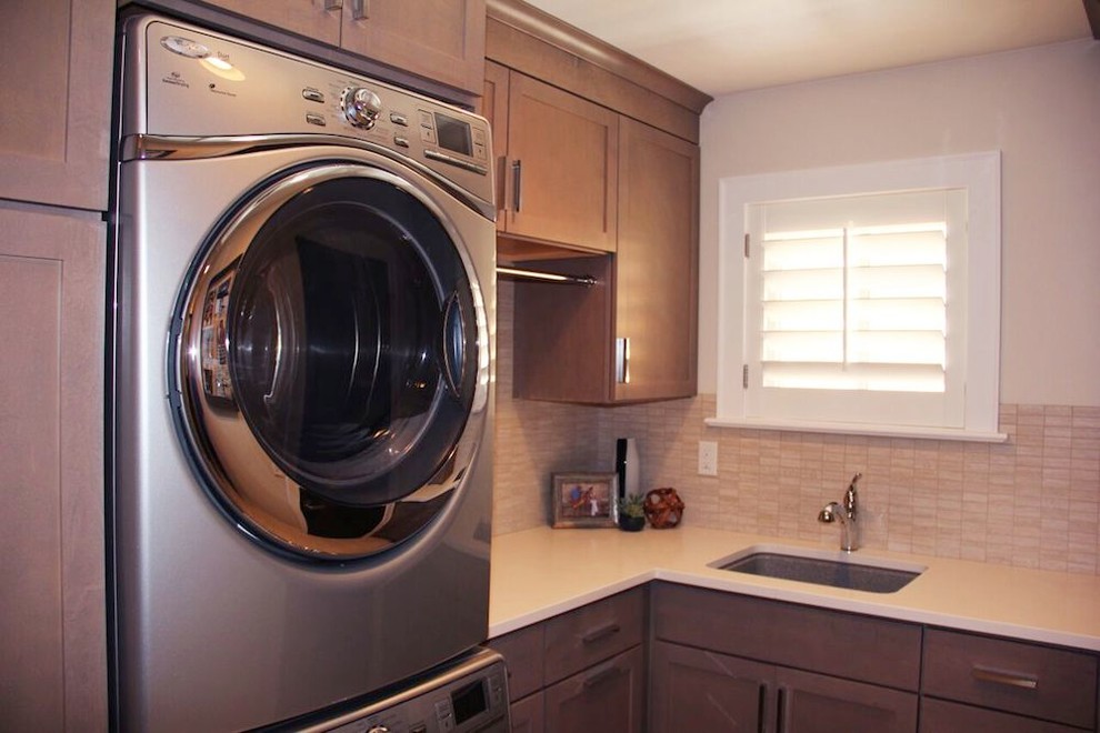 This is an example of a transitional dedicated laundry room in Denver with recessed-panel cabinets, a stacked washer and dryer, a drop-in sink, grey cabinets, quartz benchtops, white walls and ceramic floors.