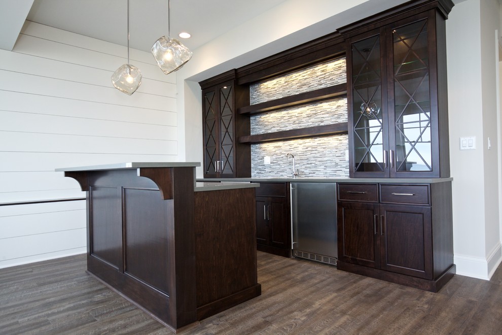 Photo of a large transitional single-wall wet bar in Chicago with an undermount sink, shaker cabinets, dark wood cabinets, solid surface benchtops, multi-coloured splashback, matchstick tile splashback and light hardwood floors.