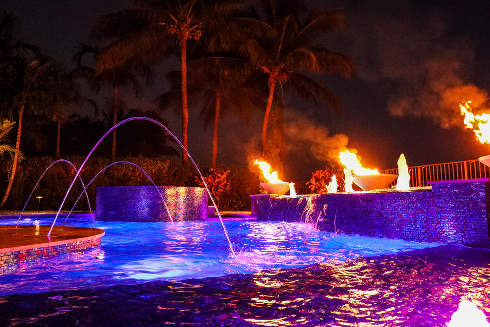 Inspiration for a large tropical backyard custom-shaped natural pool in Miami with natural stone pavers.