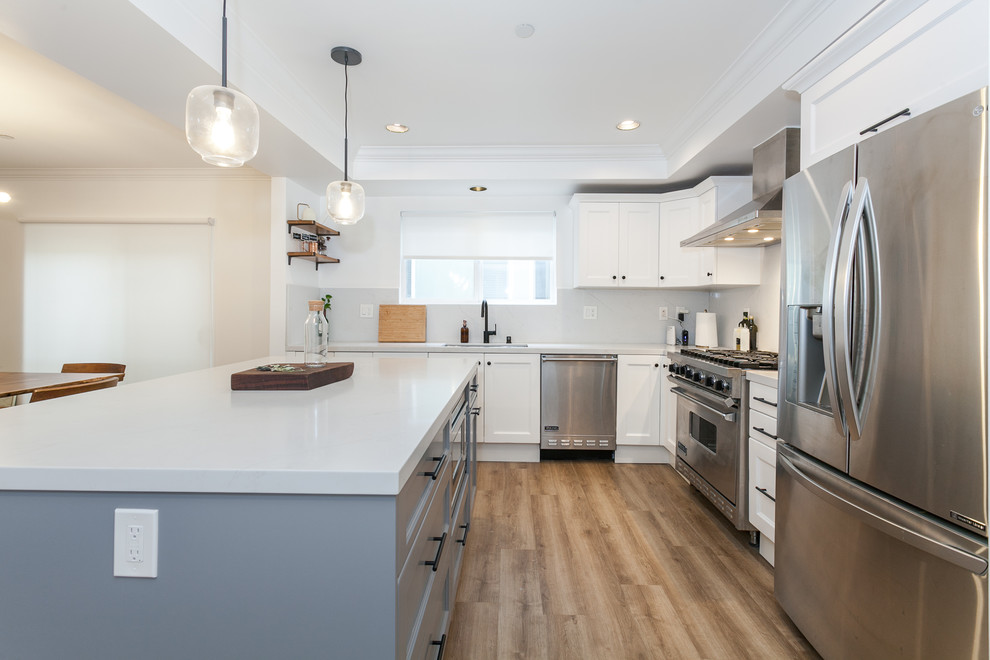 Inspiration for a mid-sized modern l-shaped eat-in kitchen in Los Angeles with an undermount sink, beaded inset cabinets, white cabinets, quartz benchtops, white splashback, porcelain splashback, stainless steel appliances, vinyl floors, with island, brown floor and white benchtop.