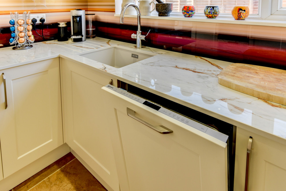 This is an example of a mid-sized u-shaped open plan kitchen in Sussex with an undermount sink, shaker cabinets, beige cabinets, multi-coloured splashback, glass sheet splashback, panelled appliances, vinyl floors, no island, brown floor and grey benchtop.