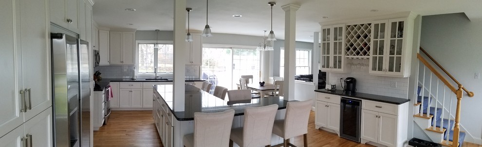 Inspiration for a large transitional l-shaped light wood floor and brown floor eat-in kitchen remodel with an undermount sink, shaker cabinets, white cabinets, granite countertops, white backsplash, subway tile backsplash, stainless steel appliances and an island