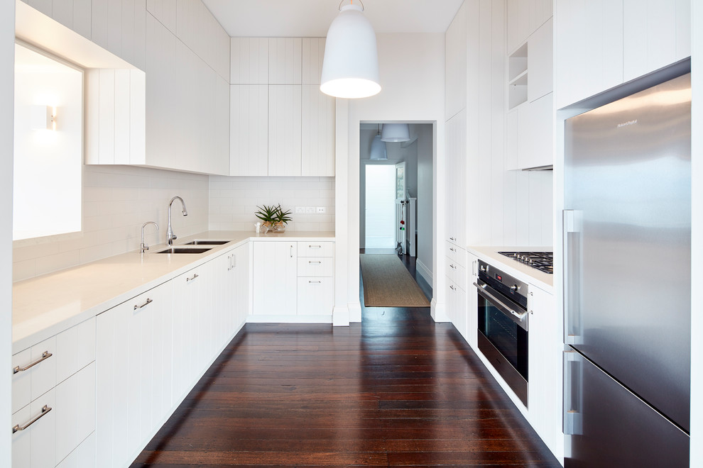 This is an example of a large transitional open plan kitchen in Sydney with white cabinets, quartz benchtops and white splashback.