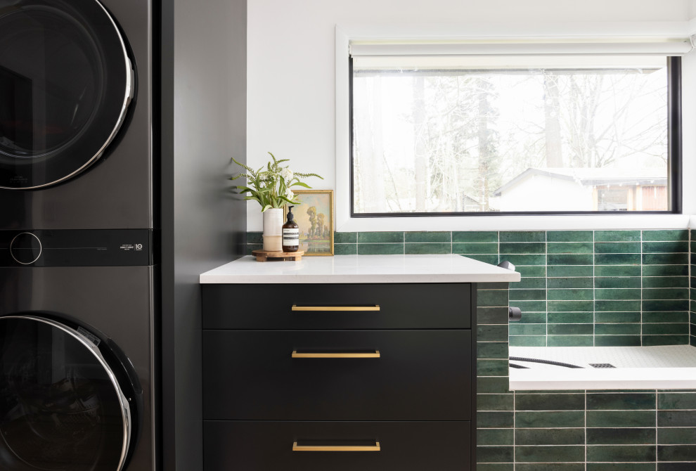 Mid-sized contemporary single-wall utility room in Portland with flat-panel cabinets, black cabinets, quartz benchtops, green splashback, cement tile splashback, white walls, light hardwood floors, a stacked washer and dryer and white benchtop.