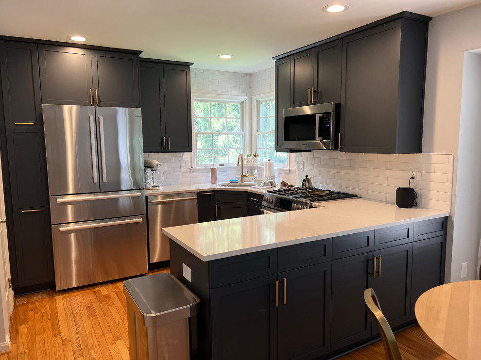 Example of a small transitional u-shaped medium tone wood floor and brown floor open concept kitchen design in Baltimore with an undermount sink, shaker cabinets, blue cabinets, quartz countertops, white backsplash, porcelain backsplash, stainless steel appliances, a peninsula and white countertops