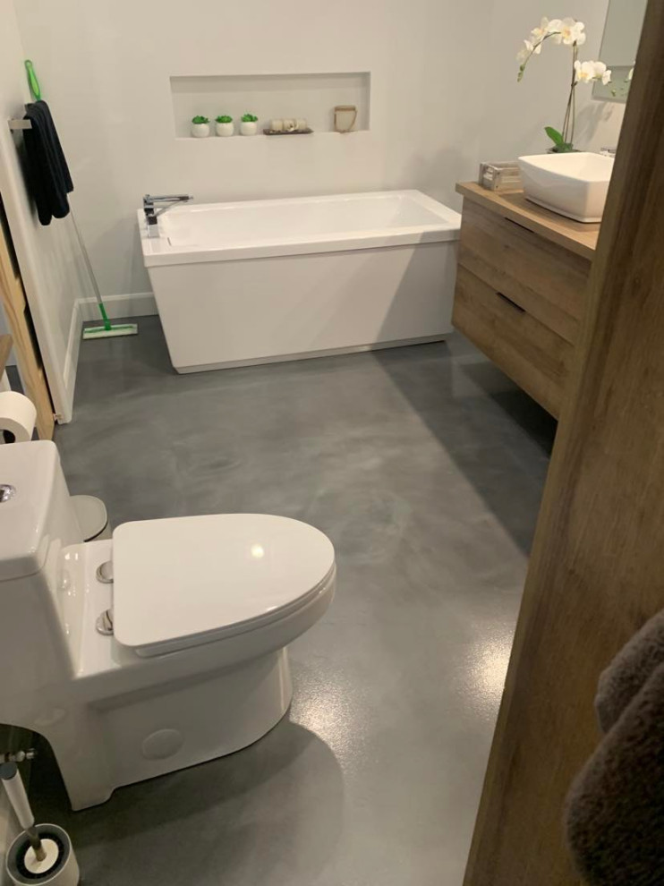 Exempel på ett brun brunt badrum med dusch, med släta luckor, skåp i mellenmörkt trä, ett fristående badkar, en toalettstol med hel cisternkåpa, vita väggar, betonggolv, ett fristående handfat, träbänkskiva och grått golv
