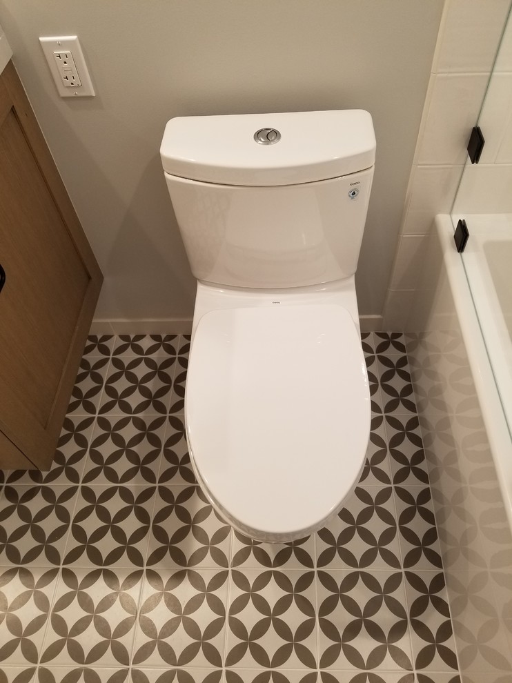 This is an example of a mid-sized modern 3/4 bathroom in Los Angeles with shaker cabinets, light wood cabinets, an alcove tub, a shower/bathtub combo, a one-piece toilet, ceramic tile, beige walls, porcelain floors, an undermount sink, solid surface benchtops, multi-coloured floor, a hinged shower door and beige benchtops.