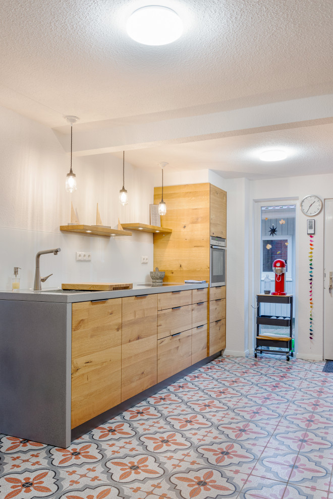 Example of a mid-sized danish galley porcelain tile and wallpaper ceiling open concept kitchen design in Hamburg with an undermount sink, flat-panel cabinets, medium tone wood cabinets, concrete countertops, white backsplash, glass sheet backsplash, stainless steel appliances and no island