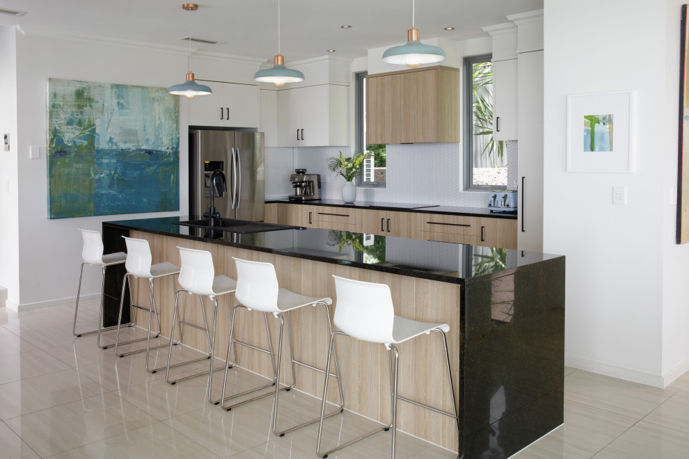 Photo of a mid-sized contemporary single-wall eat-in kitchen in Brisbane with a drop-in sink, flat-panel cabinets, medium wood cabinets, granite benchtops, white splashback, ceramic splashback, black appliances, porcelain floors, with island, beige floor and black benchtop.