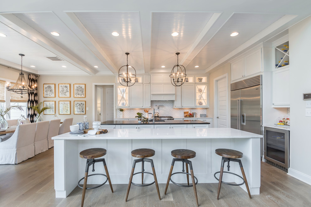 Inspiration for a transitional l-shaped eat-in kitchen in Other with an undermount sink, recessed-panel cabinets, white cabinets, white splashback, stainless steel appliances, medium hardwood floors, multiple islands, brown floor and white benchtop.