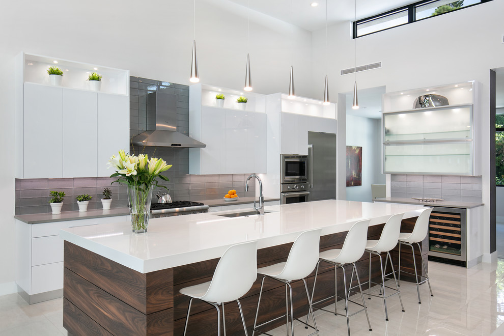 This is an example of a large modern l-shaped open plan kitchen in Tampa with an undermount sink, flat-panel cabinets, white cabinets, quartz benchtops, grey splashback, glass tile splashback, stainless steel appliances, porcelain floors, with island, white floor and grey benchtop.