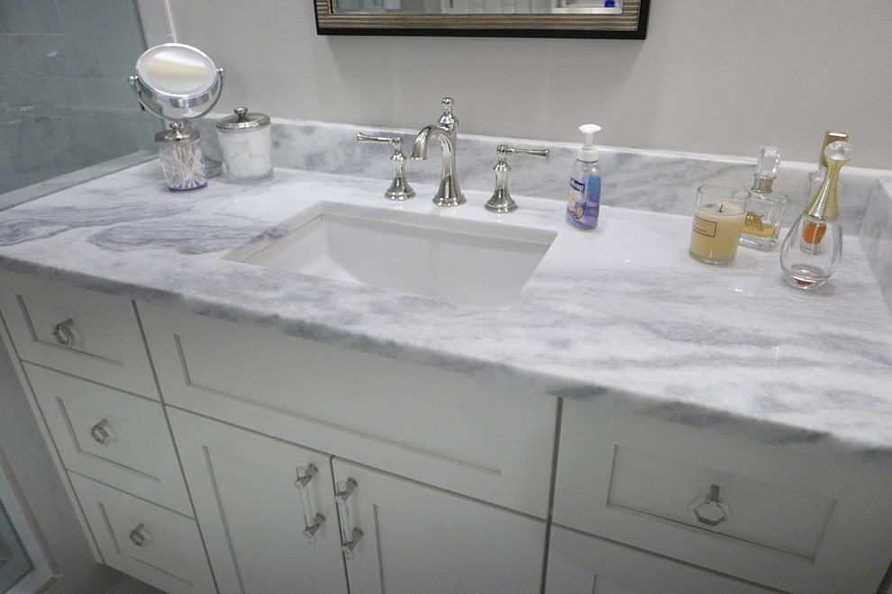 Large transitional master white tile and porcelain tile porcelain tile and white floor freestanding bathtub photo with shaker cabinets, white cabinets, a two-piece toilet, beige walls, an undermount sink, marble countertops, a hinged shower door and white countertops