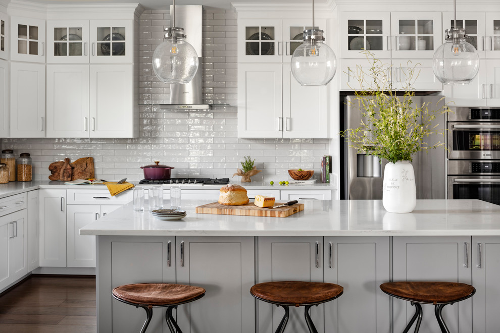 Inspiration for a large country l-shaped eat-in kitchen in DC Metro with a farmhouse sink, white cabinets, quartz benchtops, white splashback, subway tile splashback, stainless steel appliances, dark hardwood floors, with island, brown floor, white benchtop and shaker cabinets.