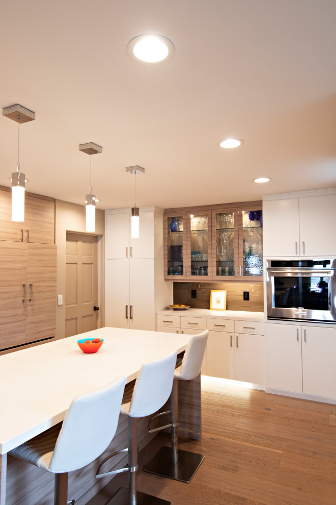 Photo of a large modern u-shaped eat-in kitchen in San Diego with an undermount sink, flat-panel cabinets, light wood cabinets, quartz benchtops, beige splashback, glass tile splashback, stainless steel appliances, light hardwood floors, with island, beige floor and white benchtop.