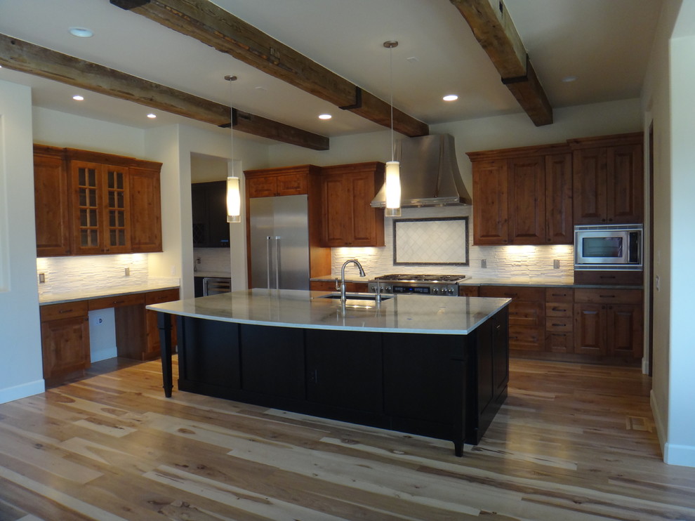 Open concept kitchen - rustic l-shaped light wood floor open concept kitchen idea in Denver with an undermount sink, recessed-panel cabinets, black cabinets, quartzite countertops, white backsplash, stone tile backsplash, stainless steel appliances, beige walls and an island