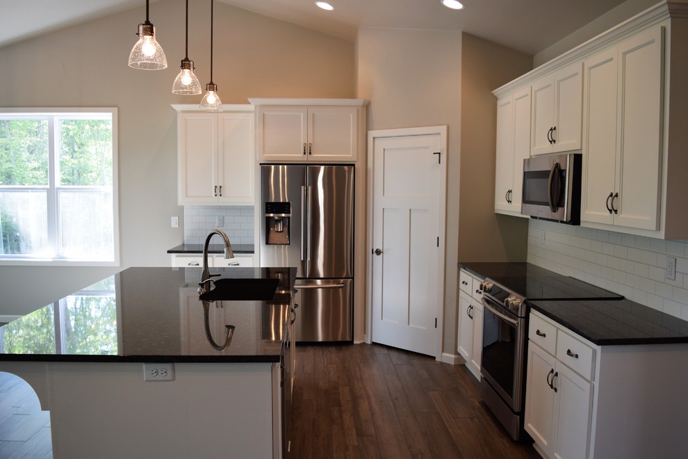 Mid-sized medium tone wood floor open concept kitchen photo with white cabinets, granite countertops, subway tile backsplash, stainless steel appliances and an island