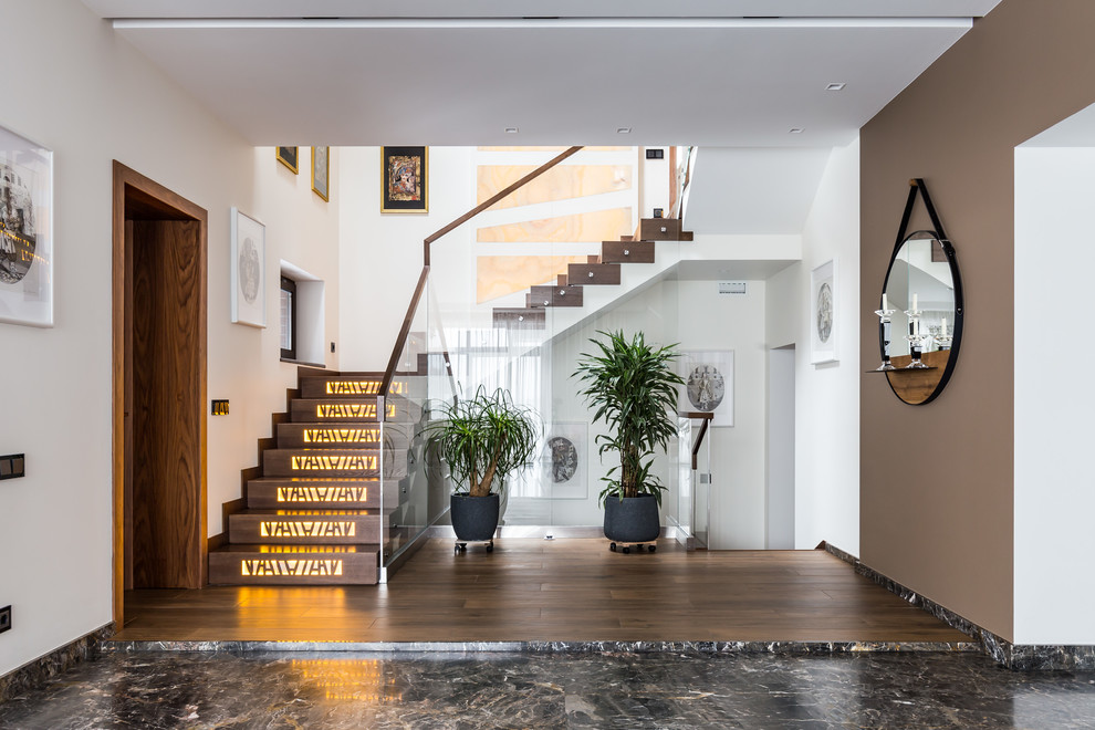 Photo of a mid-sized contemporary concrete u-shaped staircase in Saint Petersburg with marble risers and glass railing.