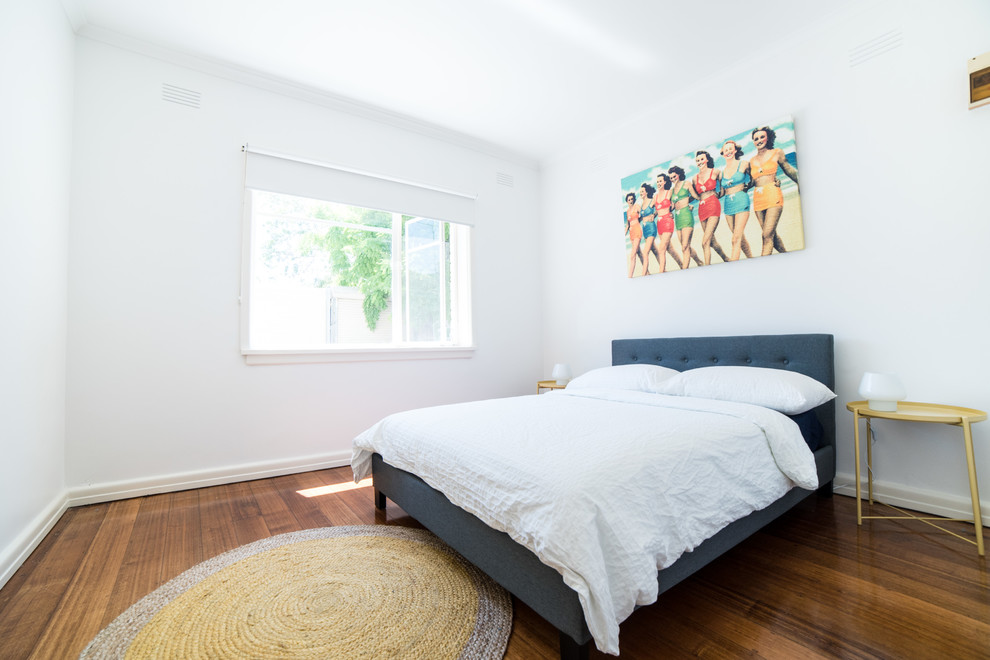 Design ideas for a beach style guest bedroom in Melbourne with white walls, medium hardwood floors and brown floor.