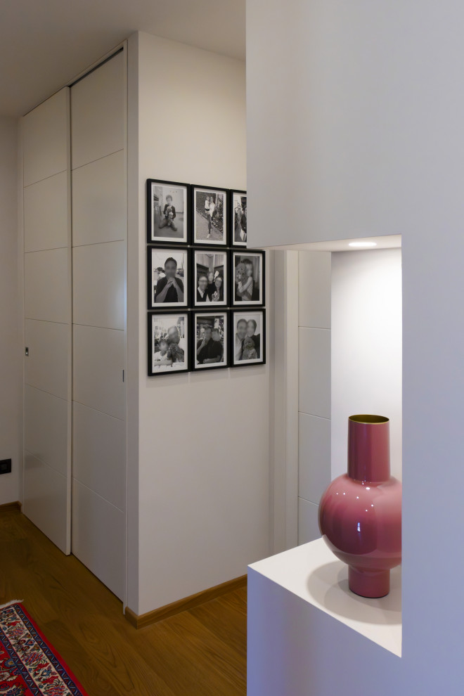Photo of a mid-sized modern hallway in Turin with white walls, light hardwood floors, brown floor and recessed.