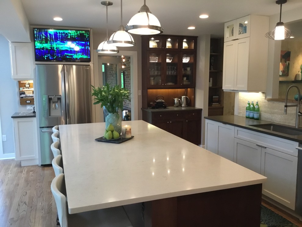 Inspiration for a mid-sized transitional u-shaped kitchen pantry in Tampa with an undermount sink, shaker cabinets, white cabinets, quartzite benchtops, beige splashback, ceramic splashback, stainless steel appliances, medium hardwood floors, with island and brown floor.