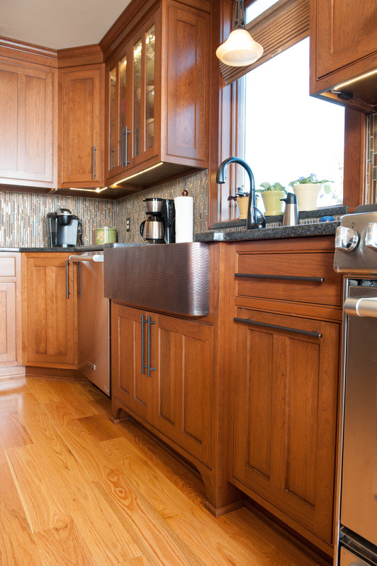Example of a mid-sized transitional l-shaped medium tone wood floor eat-in kitchen design in Orange County with a farmhouse sink, shaker cabinets, medium tone wood cabinets, granite countertops, multicolored backsplash, matchstick tile backsplash, stainless steel appliances and an island