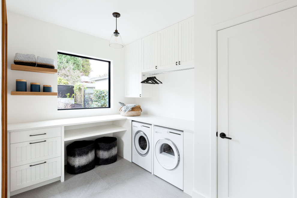 Inspiration for a medium sized farmhouse l-shaped separated utility room in Vancouver with white cabinets, white splashback, white walls, porcelain flooring, a side by side washer and dryer, grey floors and white worktops.