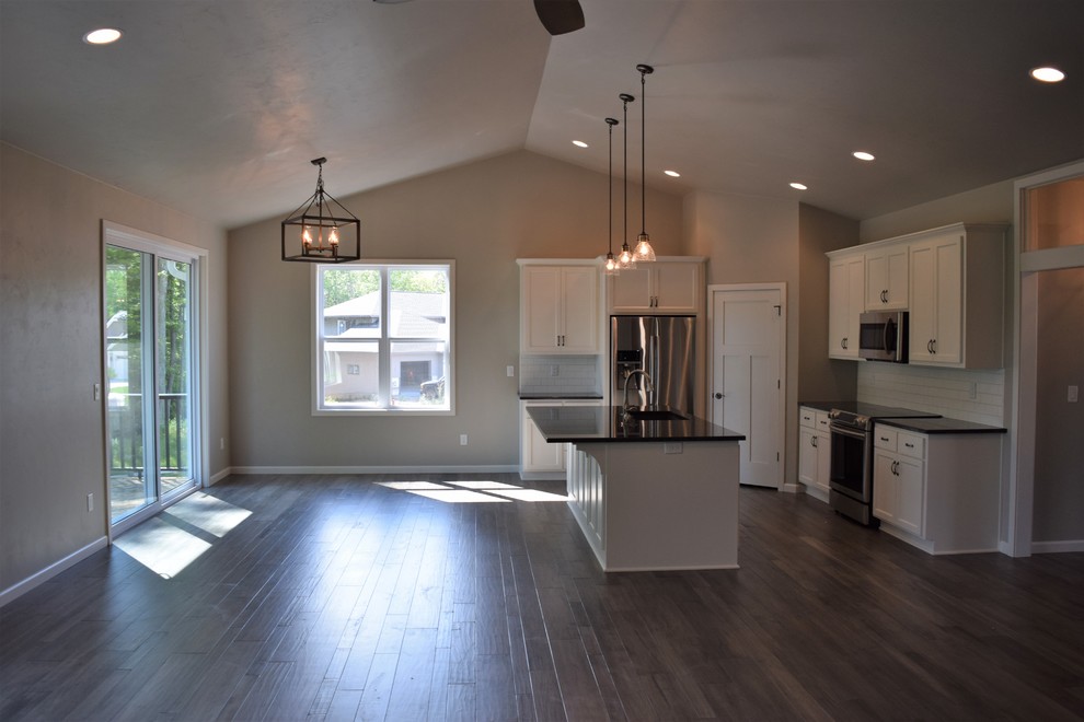 Example of a mid-sized medium tone wood floor open concept kitchen design with white cabinets, granite countertops, subway tile backsplash, stainless steel appliances and an island