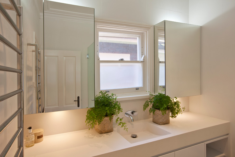 Inspiration for a large transitional kids bathroom in Sydney with an integrated sink, flat-panel cabinets, white cabinets, solid surface benchtops, a corner shower, a one-piece toilet, beige tile, stone tile and white walls.