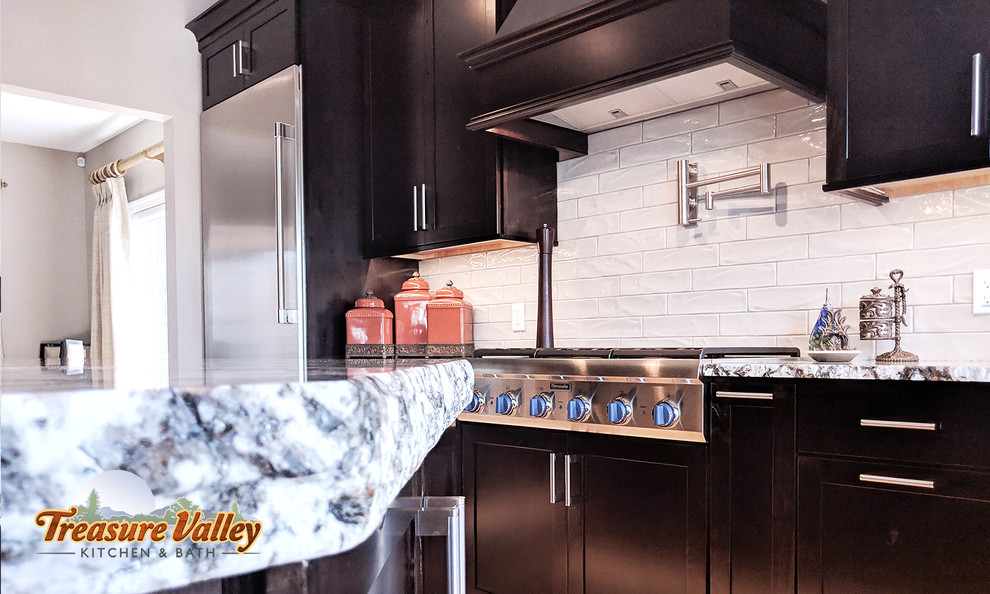Example of a mid-sized transitional l-shaped light wood floor open concept kitchen design in Boise with a farmhouse sink, shaker cabinets, granite countertops, glass tile backsplash, stainless steel appliances and an island
