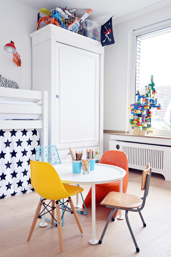 Mid-sized scandinavian gender-neutral kids' bedroom in Dusseldorf with white walls and light hardwood floors for kids 4-10 years old.