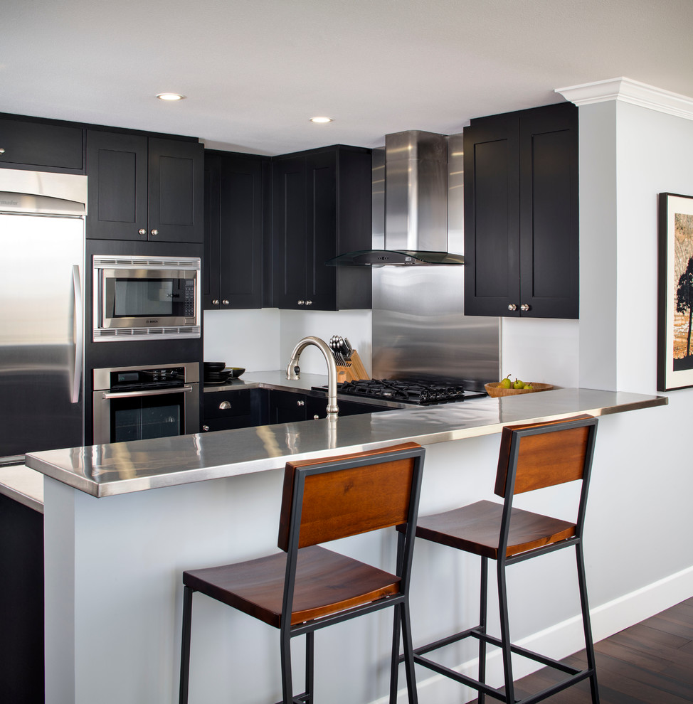 Inspiration for a small modern u-shaped open plan kitchen in San Francisco with a double-bowl sink, shaker cabinets, black cabinets, stainless steel benchtops, metallic splashback, metal splashback, stainless steel appliances, dark hardwood floors and a peninsula.