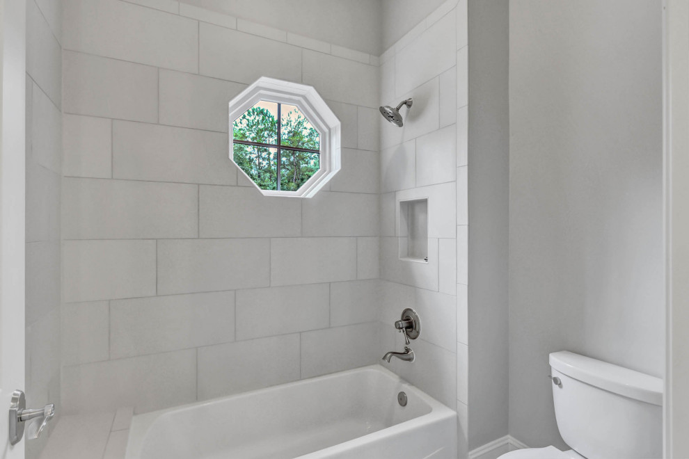 Modelo de cuarto de baño infantil de tamaño medio con bañera empotrada, combinación de ducha y bañera, sanitario de una pieza, baldosas y/o azulejos grises, paredes grises y hornacina