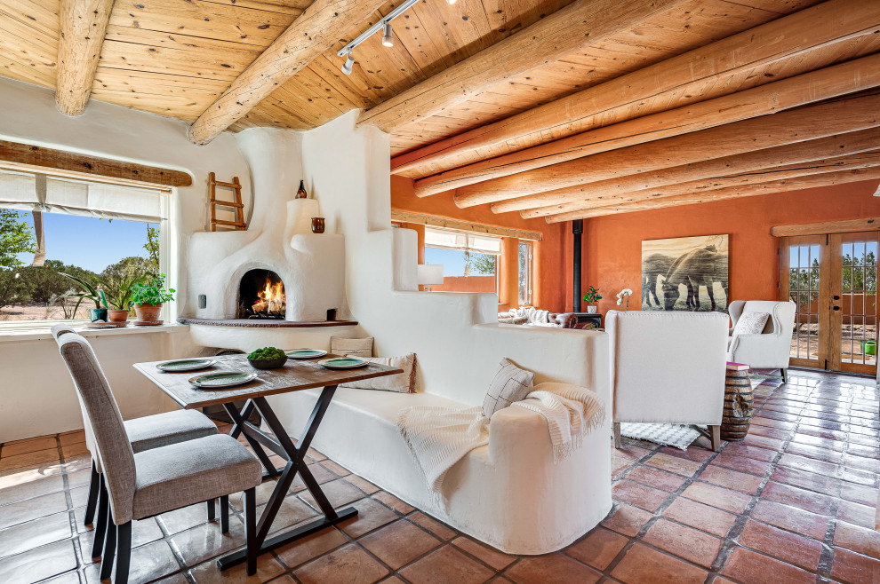 Medium sized dining room in Other with banquette seating, white walls, terracotta flooring, a corner fireplace, a plastered fireplace surround, orange floors and exposed beams.