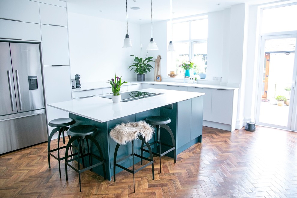 Design ideas for a mid-sized eclectic l-shaped eat-in kitchen in Manchester with an integrated sink, flat-panel cabinets, blue cabinets, quartzite benchtops, white splashback, stainless steel appliances, dark hardwood floors, with island, brown floor and white benchtop.