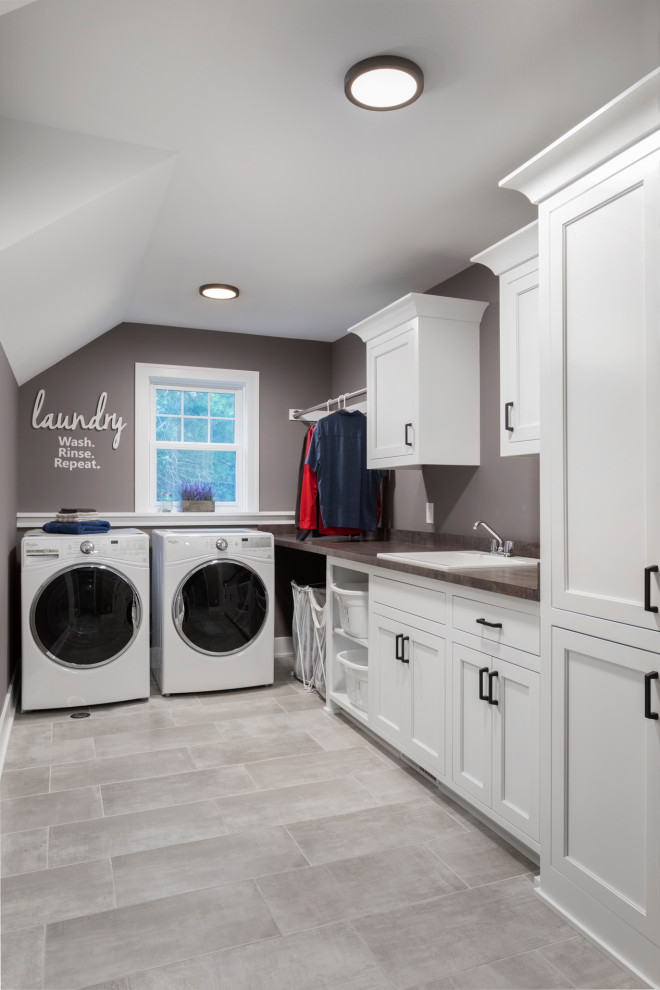 Inspiration for a mid-sized transitional galley dedicated laundry room in Milwaukee with a drop-in sink, shaker cabinets, white cabinets, grey walls, a side-by-side washer and dryer, grey floor, brown benchtop, laminate benchtops and ceramic floors.