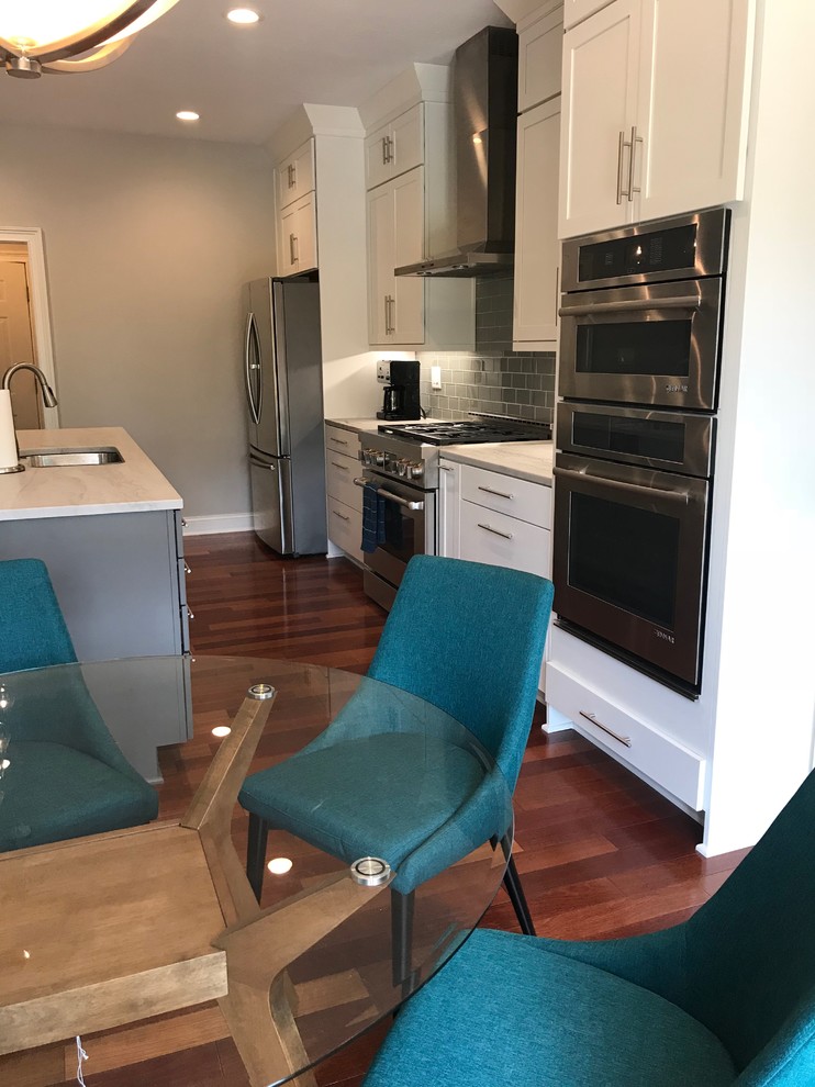 Example of a mid-sized transitional single-wall medium tone wood floor and brown floor eat-in kitchen design with an undermount sink, shaker cabinets, white cabinets, quartzite countertops, gray backsplash, glass tile backsplash, stainless steel appliances, an island and multicolored countertops