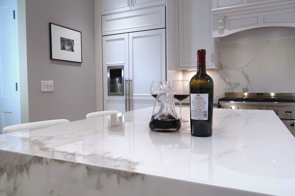 Inspiration for a small transitional u-shaped light wood floor and brown floor enclosed kitchen remodel with a farmhouse sink, recessed-panel cabinets, white cabinets, quartz countertops, white backsplash, stone slab backsplash, stainless steel appliances, an island and white countertops
