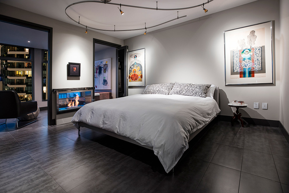 This is an example of a mid-sized modern master bedroom in San Diego with grey walls, ceramic floors, a two-sided fireplace, a stone fireplace surround and grey floor.