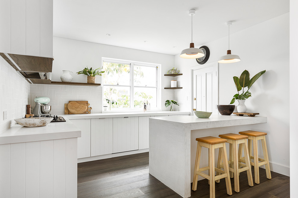 Inspiration for a mid-sized beach style l-shaped kitchen pantry in Sydney with an undermount sink, shaker cabinets, white cabinets, quartz benchtops, beige splashback, ceramic splashback, white appliances, dark hardwood floors, with island, brown floor and white benchtop.