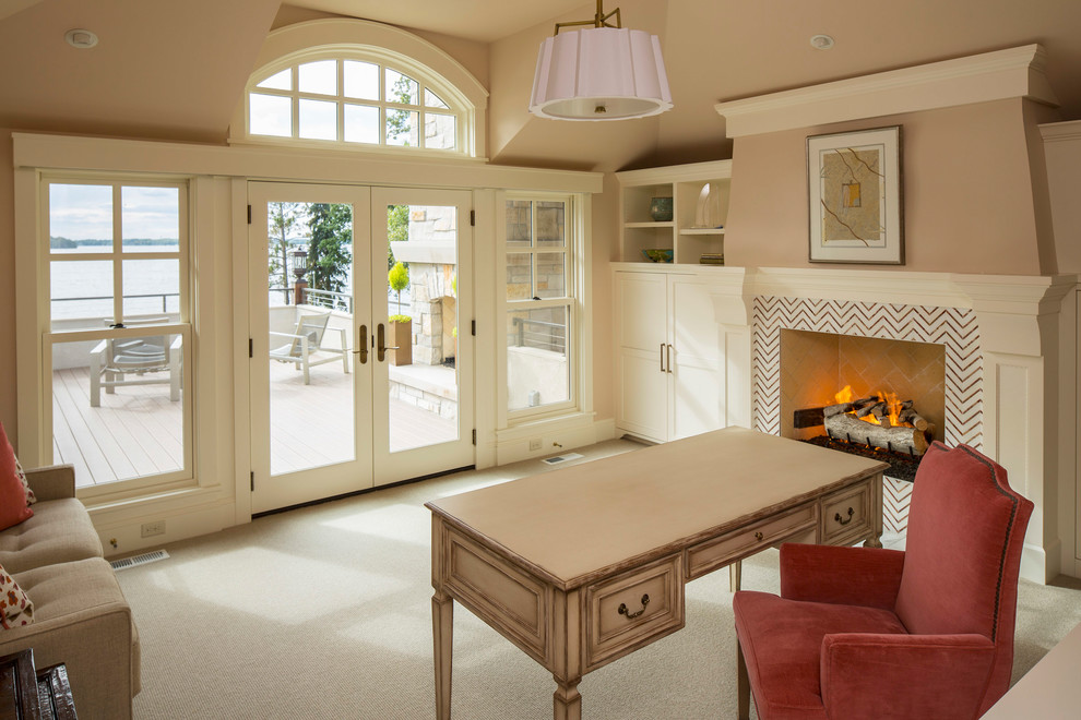 Photo of a beach style study room in Minneapolis with beige walls, carpet, a standard fireplace, a tile fireplace surround, a freestanding desk and beige floor.