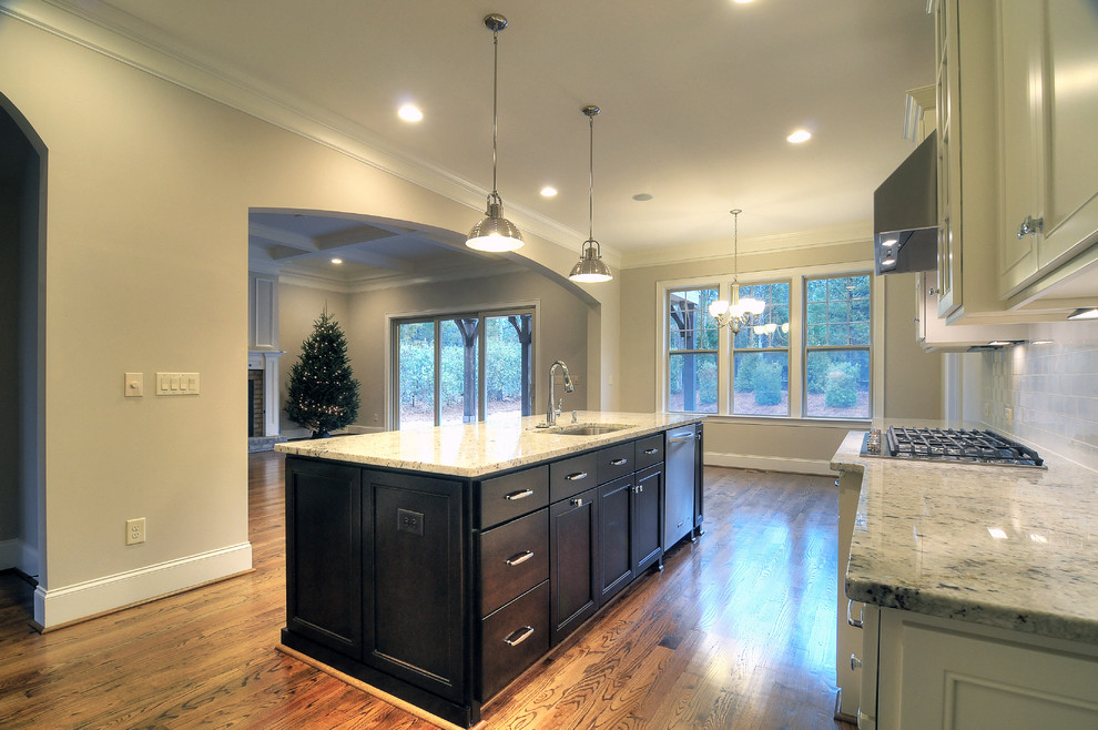 Large transitional l-shaped medium tone wood floor open concept kitchen photo in Charlotte with an undermount sink, recessed-panel cabinets, white cabinets, granite countertops, white backsplash, subway tile backsplash, stainless steel appliances and an island